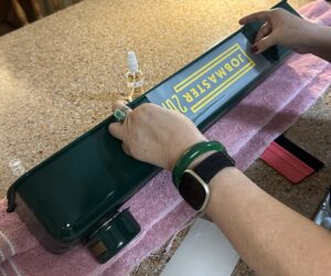 Hands applying a yellow JOBMASTER 2024 vinyl decal onto a green valve cover as part of a custom graphics project.